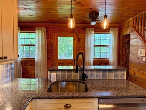 A kitchen with granite countertops, a stainless steel sink, wooden walls, and a ceiling fan.