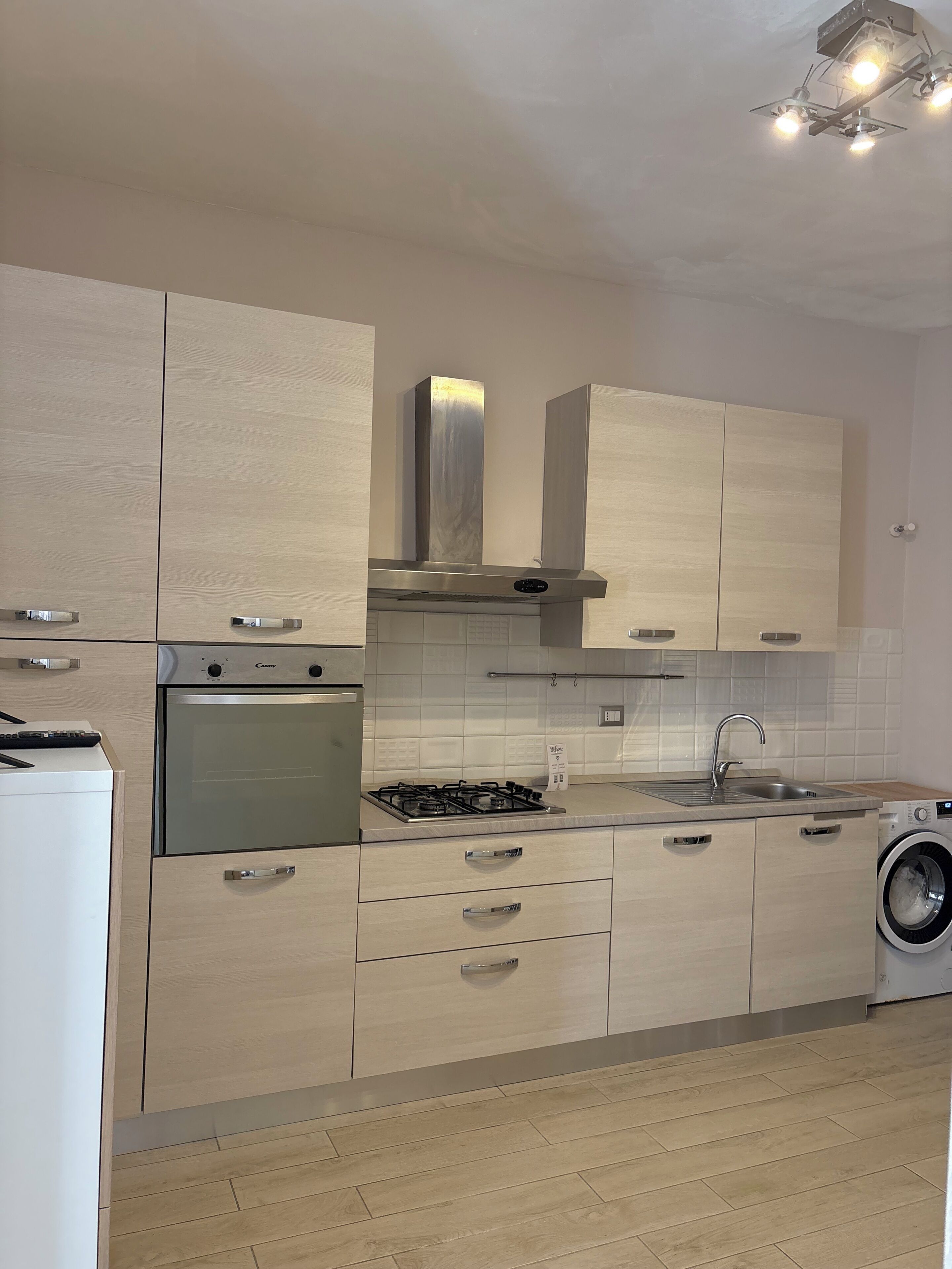 A modern kitchen with a built-in oven, gas stove, stainless steel range hood, and a washing machine.