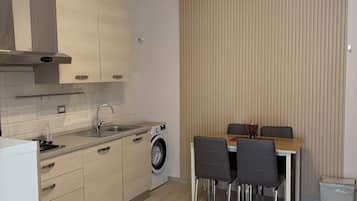 Une cuisine moderne équipée d’un lave-linge intégré, un coin repas avec une table et des chaises, et un mur recouvert de stores verticaux.