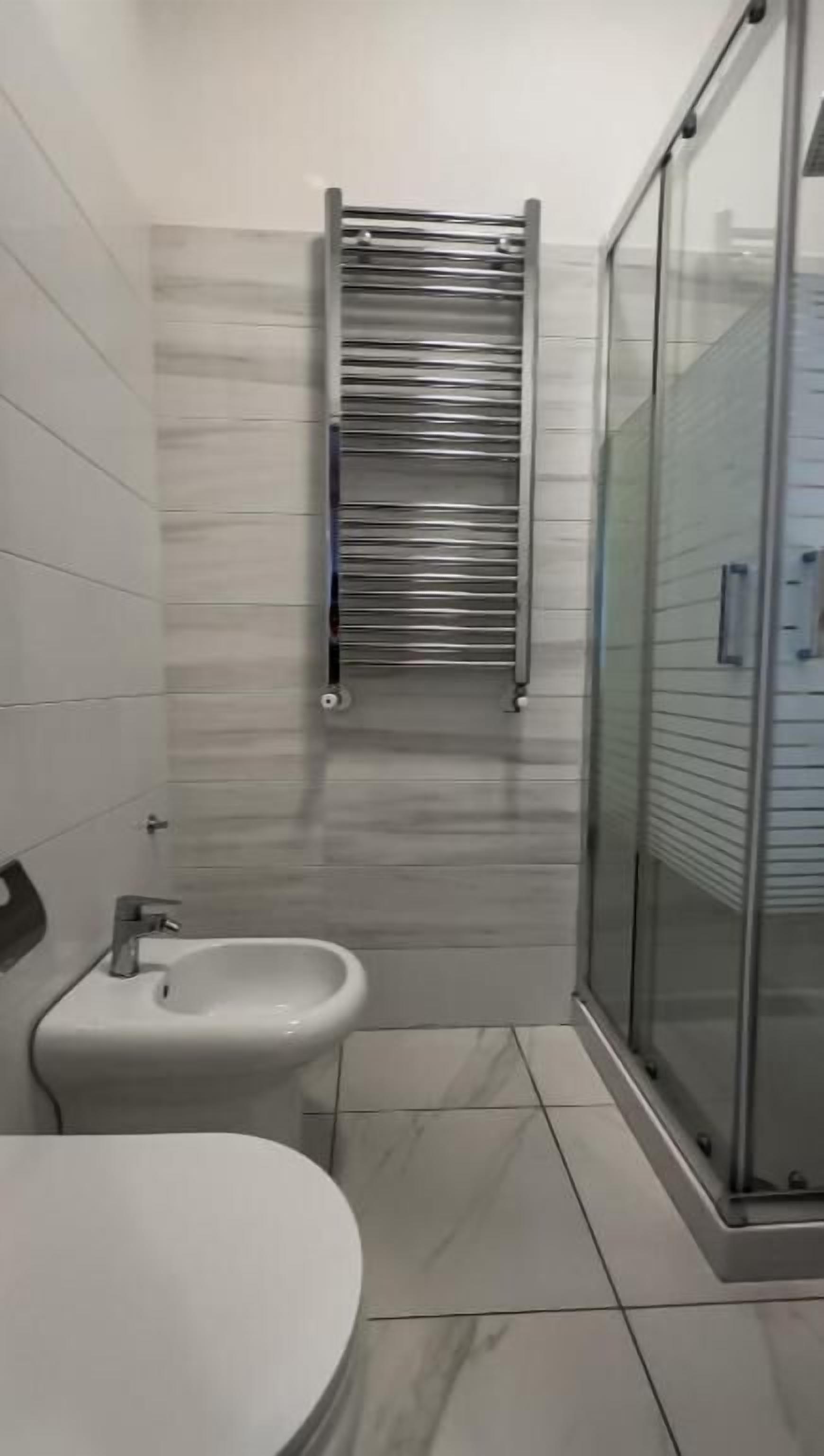 A bathroom with a bidet, a glass shower enclosure, and a towel rack.