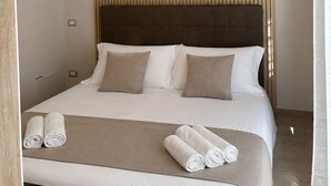 A hotel room with a bed, pillows, a headboard, a hanging light fixture, and rolled towels on the bed. - IL PALAZZETTO GAETA (Gaeta)