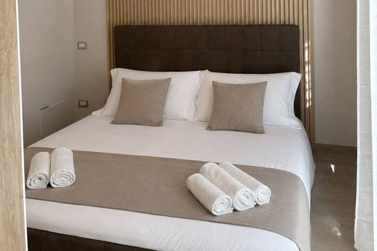 Ein Hotelzimmer mit Bett, Kissen, Kopfteil, einer Pendelleuchte und aufgerollten Handtüchern auf dem Bett.