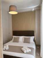Camera d'albergo con un letto, cuscini, testiera e una lampada a sospensione, con asciugamani arrotolati sul letto.