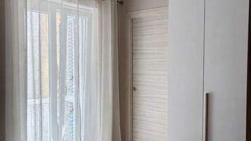 Camera d'albergo con un letto, un armadio capiente, un condizionatore a soffitto e una finestra con tende leggere.