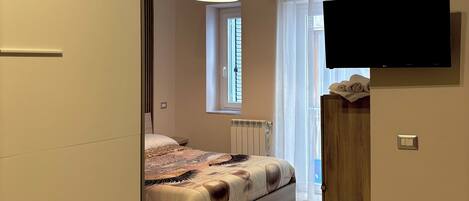 Un dormitorio con cama, televisión montada en la pared, ventana con cortinas y aire acondicionado.
