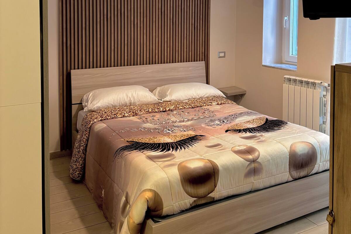Ein modernes Schlafzimmer mit Bett, einer Pendelleuchte, einem Fenster und einem an der Wand befestigten Fernseher.