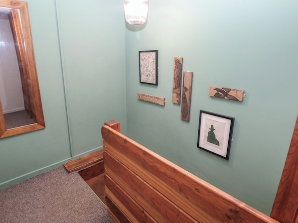 Un pasillo con un banco de madera, un espejo y obras de arte en la pared, incluyendo un cuadro enmarcado y placas de madera.