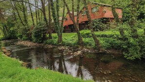 Eine rote Holzhütte vor einem Fluss, umgeben von Bäumen und Grün.