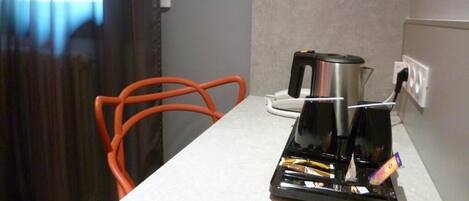 Una pequeña cocina americana con cafetera, hervidor de agua y tostadora sobre una encimera blanca.