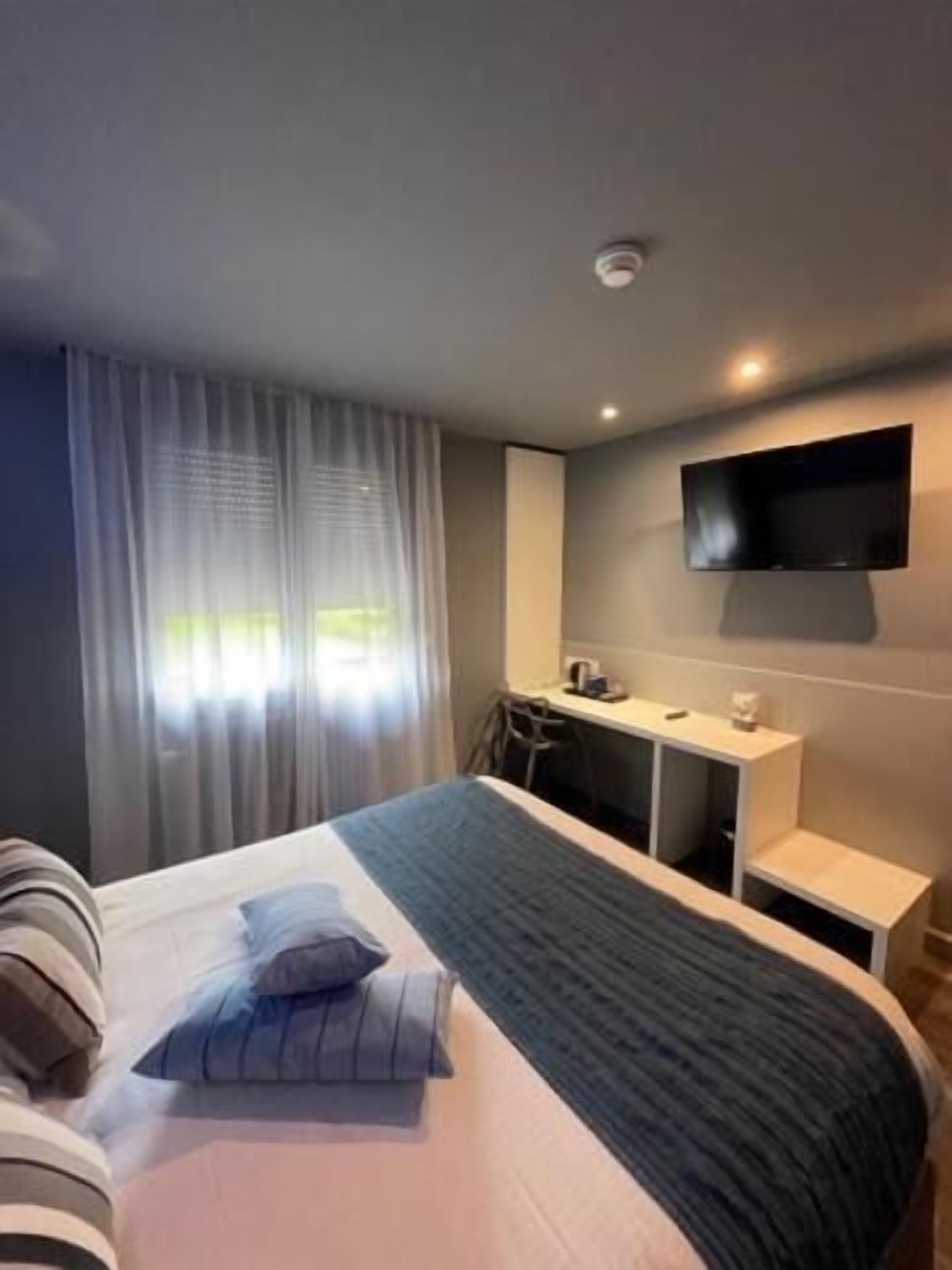Habitación de hotel con cama, escritorio, silla, televisión y ventana con cortinas.