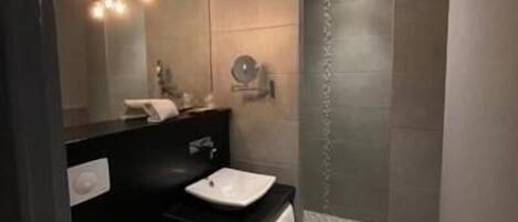 A modern bathroom with a black vanity, white sink, and a separate shower area.