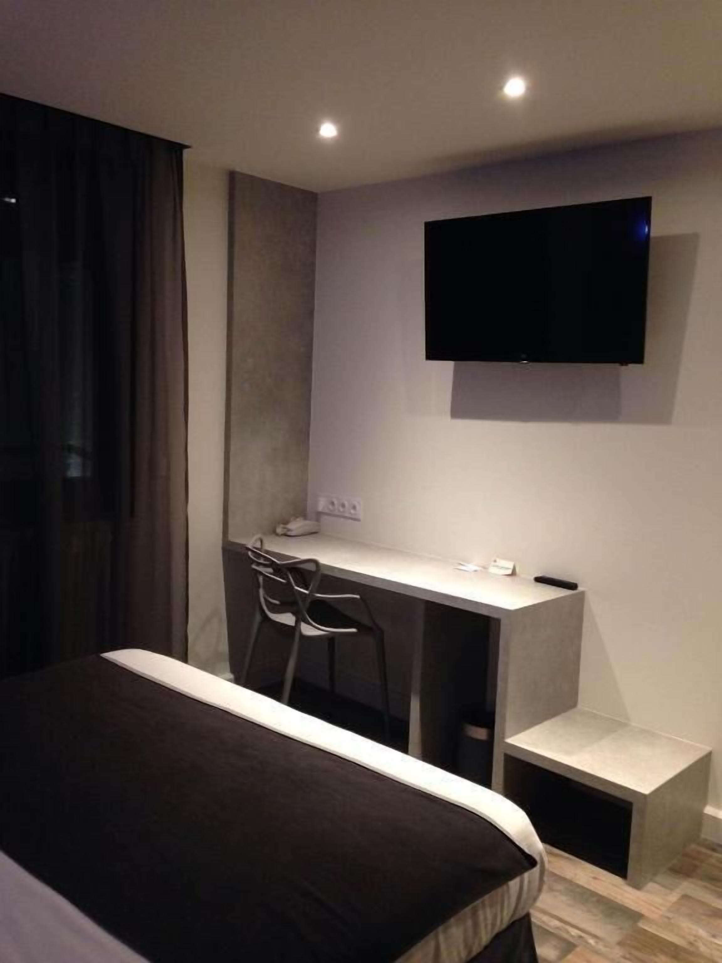 Una habitación de hotel con cama, escritorio, silla, televisor montado en la pared y una mesita.