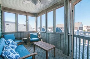 Un espacio al aire libre techado con piso de madera, un sofá con cojines azules, una mesa y sillas.