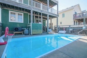 A swimming pool with a basketball hoop, a covered patio area, and a two-story building with a balcony. - Haven House-Heated Pool, Spa, Views, 1 blk to sea (Kill Devil Hills)