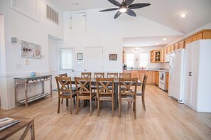 A spacious kitchen with wooden cabinets, a dining table with chairs, and a ceiling fan. - Haven House-Heated Pool, Spa, Views, 1 blk to sea (Kill Devil Hills)