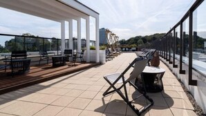 Eine Außenterrasse mit Liegestühlen, einer Pergola und Blick auf die Stadtlandschaft.