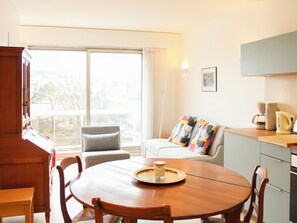 Un coin repas avec une table ronde en bois, des chaises, une machine à café et une vue sur l’extérieur grâce à une grande fenêtre.