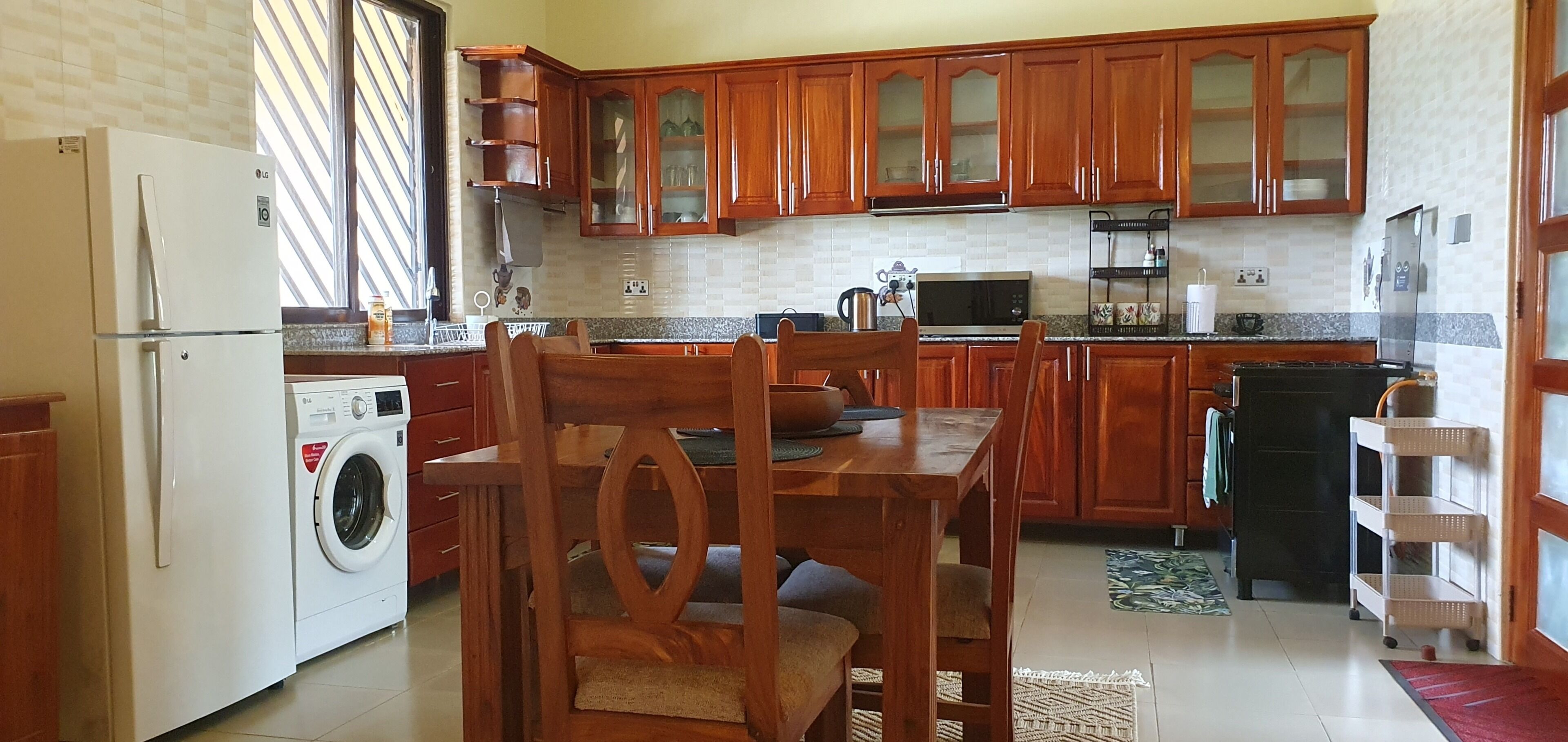 Une cuisine avec des meubles de rangement en bois, un lave-linge, une table à manger avec des chaises et un réfrigérateur.
