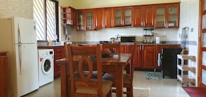 A kitchen with wooden cabinets, a washing machine, a dining table with chairs, and a refrigerator.