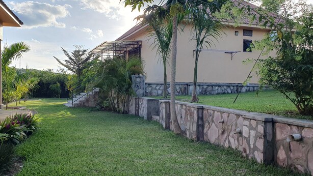 Una propiedad residencial con un muro de piedra, un césped y una casa con techo de tejas.