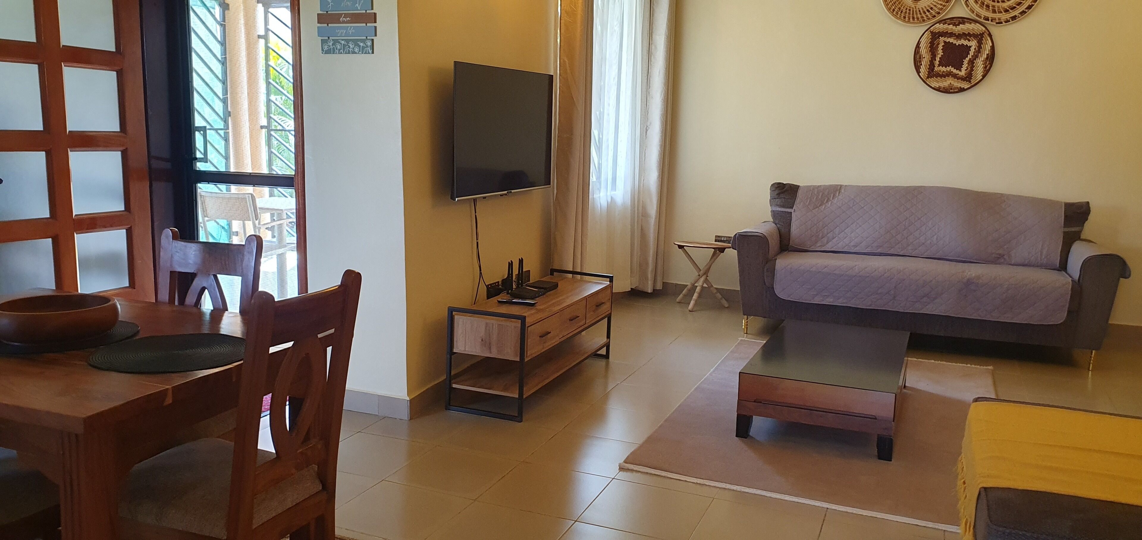 A living room with a sofa, a television, a dining table with chairs, and a window with curtains.