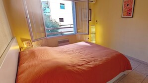 Et soveværelse med seng, vindue, radiator, spejl og et billede i ramme på væggen.