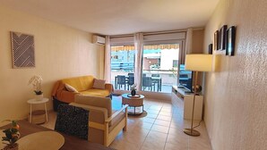 En stue med sofa, et lille bord, en lampe og udsigt til en balkon.