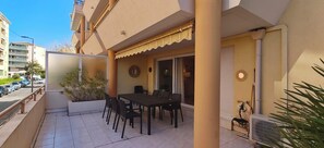 A balcony with a table and chairs, a potted plant, and a view of the street. - Large apartment with a 35 m² terrace (Saint-Raphaël)