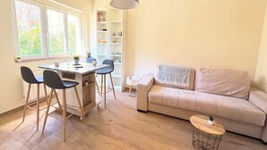 Un salon comprenant un canapé, une table à manger avec des chaises, une petite table d’appoint, un luminaire suspendu et une bibliothèque.