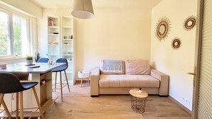 Un salon moderne comprenant un canapé, une table à manger avec des chaises, un luminaire suspendu et des œuvres d’art décoratives murales.