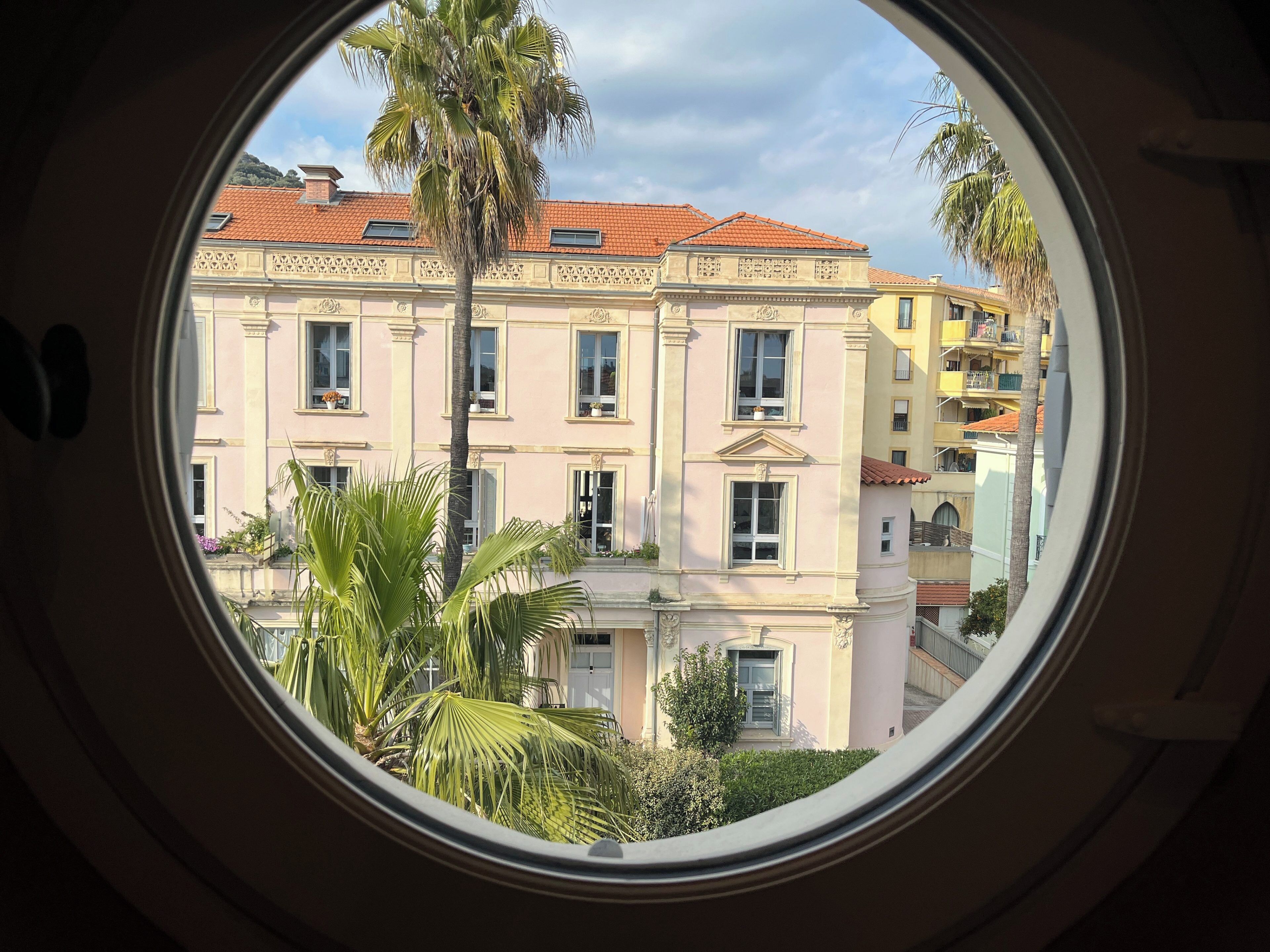 Une vue à travers la fenêtre d’un immeuble doté de nombreuses fenêtres et de balcons, entouré de verdure.