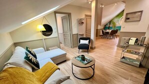 A modern living room with a sofa, ottoman, and a dining area with chairs and a table. - Chic apartment between the sea and palm trees (Hyères)