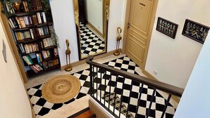 A staircase with a black and white checkered floor, a wooden bookshelf with books, a mirror, and a door labeled 'LA FAMILIA'. - Chic apartment between the sea and palm trees (Hyères)