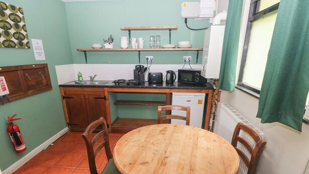 Una cocina compacta con una mesa y sillas de madera, un refrigerador pequeño y una estantería con utensilios de cocina.