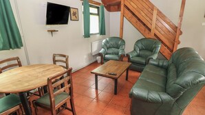 Un salón con una mesa de madera, sofá de cuero verde y sillas.
