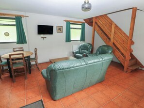 A living room with a sofa, chairs, a table, a TV, and a wooden staircase. - Cabin No. 11 - Salt and Fern Cabins (Port Talbot)
