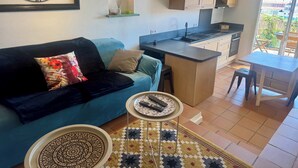 A living room with a sofa, a coffee table, a kitchen area with cabinets, a window, and a view of the outside. - Beautiful 45 m² apartment with terrace in Nice (Nice)