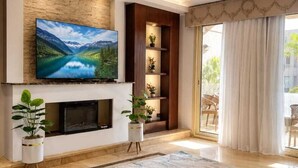 A modern living room with a fireplace, a large flat-screen TV, and a view of the outdoors. - ELITE New Modern 3BR Apartment (New Cairo)