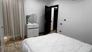 A bedroom with a bed, a vanity with a mirror, an air conditioning unit, and a door leading to another room. - ELITE New Modern 3BR Apartment (New Cairo)