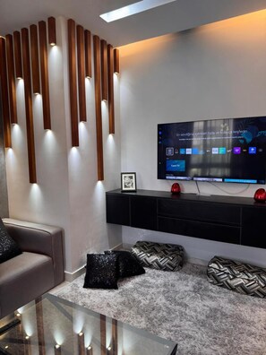 A modern living room with a flat-screen TV, a sofa, a glass coffee table, and a decorative wall panel. - ELITE New Modern 3BR Apartment (New Cairo)