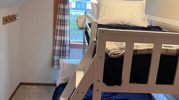 Ein Schlafsaalzimmer mit Etagenbett, einem Fenster mit Vorhängen und einer kleinen Holzablage.