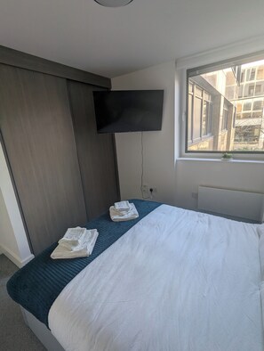 Ein Hotelzimmer mit Bett, Flachbildfernseher an der Wand und einem Fenster mit Blick auf Gebäude.