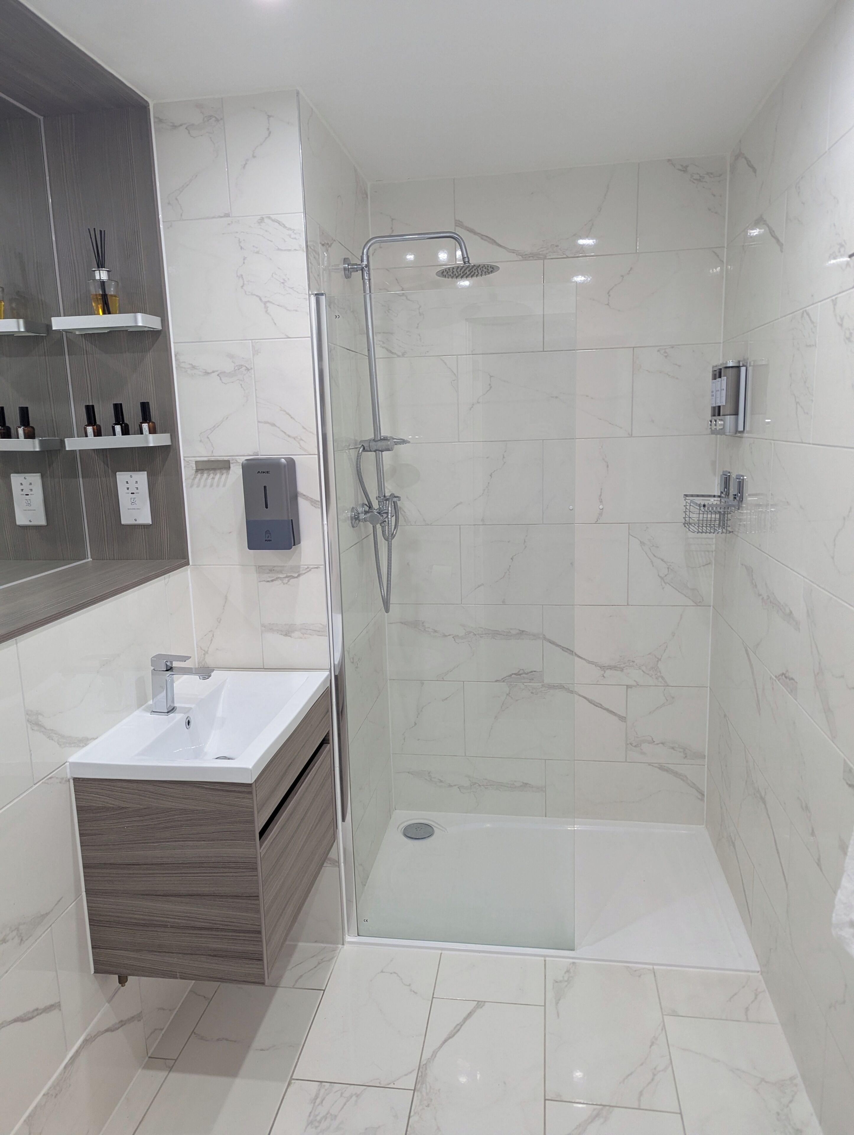 Ein modernes Badezimmer mit einer Glaskabine zur Dusche, einem Waschtisch und marmorverkleideten Wänden.