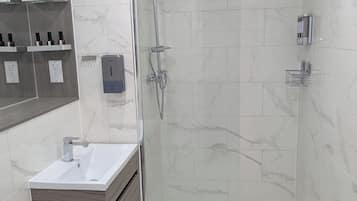 Ein modernes Badezimmer mit einer Glaskabine zur Dusche, einem Waschtisch und marmorverkleideten Wänden.