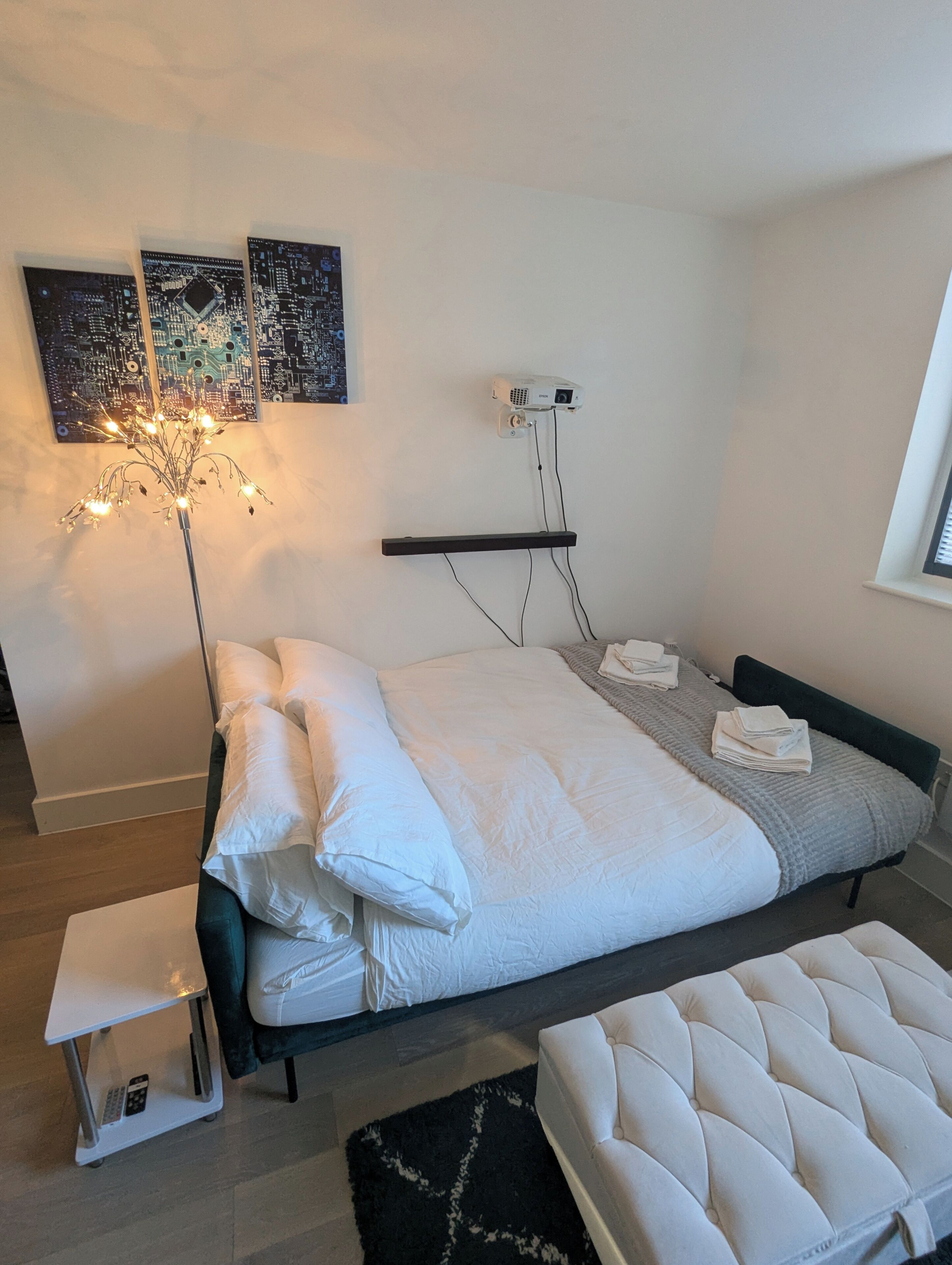 Una camera da letto moderna con un letto, un comodino e un proiettore montato a parete.