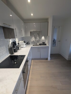 A modern kitchen with white cabinets, a black induction cooktop, and a wooden floor. - Luxury Apartment Central Milton Keynes close to Train Station (Milton Keynes)