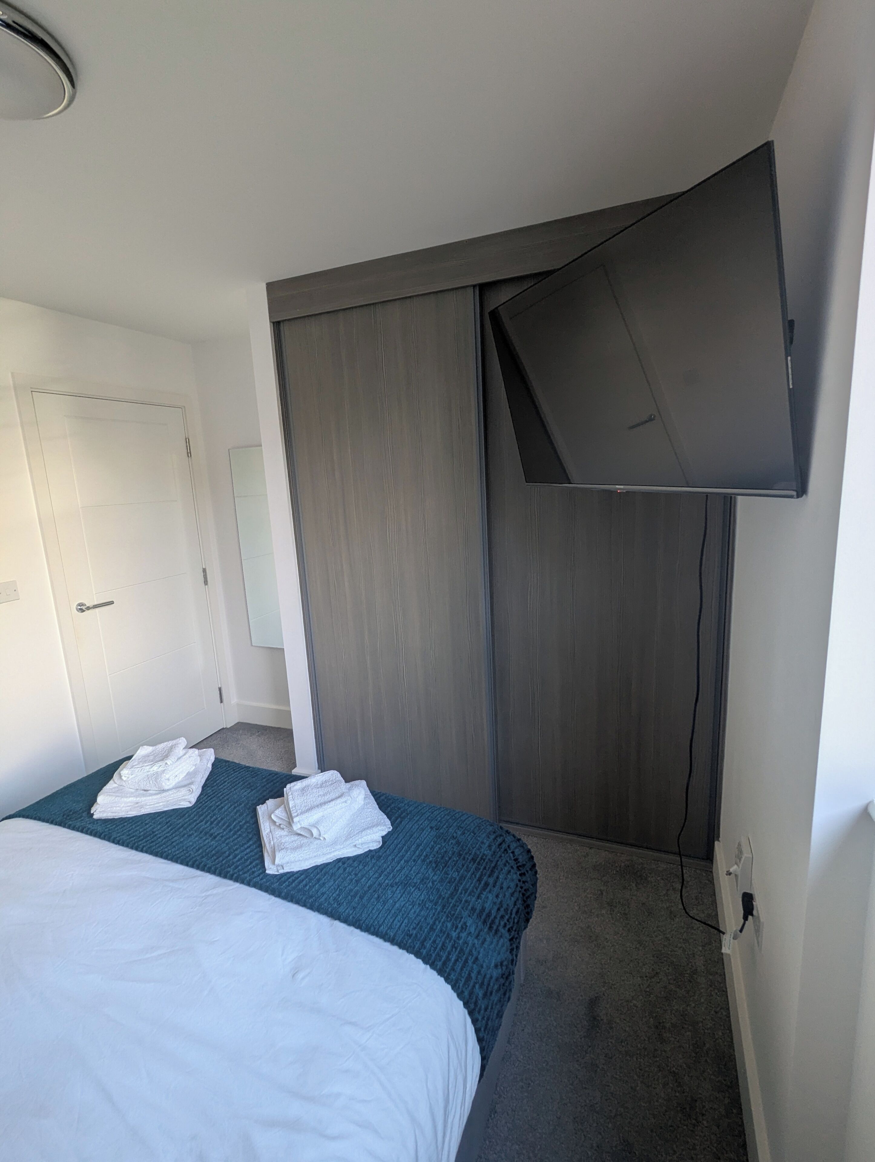 Een hotelkamer met een bed, een flatscreen televisie aan de muur, een kledingkast en een deur.
