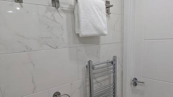 Een badkamer met witte marmeren tegels, een handdoekhouder, een handdoekwarmer en een deur.
