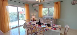 A dining area with a table set for four, chairs, a chandelier, and a window with curtains. - Thomas apartments Corfu (Corfu)