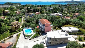 An aerial view of a residential area with a swimming pool, surrounded by greenery and houses. - Thomas apartments Corfu (Corfu)